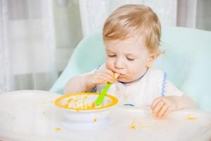 bambino-pappa-seggiolone-©-Liandstudio-_-Dreamstime.com---Smiling-Baby-Eating-Food-On-Kitchen-Photo